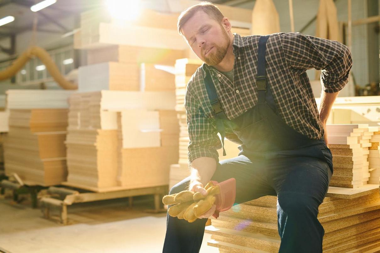 An injured worker sits at their workplace, expressing discomfort and pain