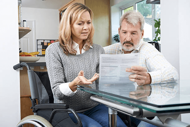 A woman in a wheelchair with a frustrated look on her face, and a man looking over a document together.